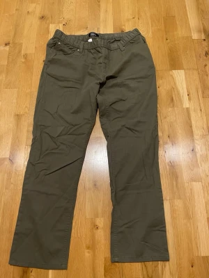 Olivgröna chinos från Bpc stl 54 - Snygga olivgröna chinos från bpc med rak passform och elastisk midja. Byxorna har klassisk design med fickor fram och är tillverkade i ett mjukt bomullstyg som känns bekvämt hela dagen.
