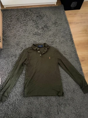 Grön långärmad skjorta från Polo Ralph Lauren - Mörkgrön långärmad skjorta från Polo Ralph Lauren med klassisk krage, knappar framtill och broderad logga på bröstet. Slim fit-modell som passar perfekt till en avslappnad men ändå stilren look.