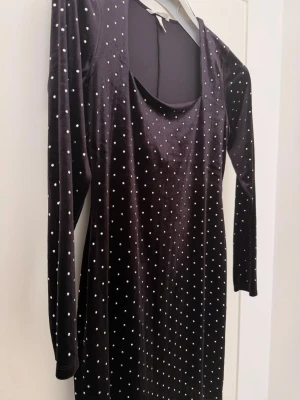 Svart klänning från H&M - Snygg svart klänning från H&M med vita diamanter och lång ärm. Klänningen har en kroppsnära passform och är tillverkad i ett stretchigt material som ger en bekväm känsla. Perfekt för dig som gillar en stilren look med lite edge.