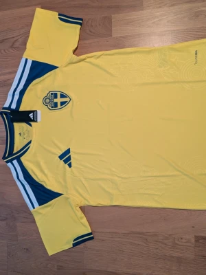 Sverige herrlandslagets matchtröja. S.m.l  - Helt ny Gul matchtröja från Adidas för Sveriges herrlandslag i fotboll. Tröjan har blå detaljer på axlar och ärmar, samt Sveriges landslagsemblem på bröstet. Materialet är lätt och andas, perfekt för träning eller match. SVERIGE-tryck i nacken.