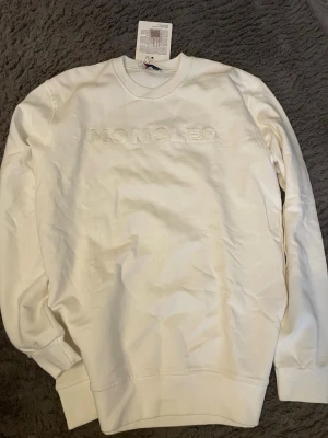 Vit sweatshirt från Moncler - Snygg vit sweatshirt från Moncler med broderad logotyp framtill. Tröjan har rund halsringning, långa ärmar och ribbade muddar vid ärmslut och nederkant. Perfekt för en clean och stilren look.