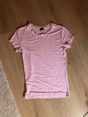 Ljusrosa t-shirt från Gina Tricot - En enkel och snygg ljusrosa t-shirt från Gina Tricot. Modellen är klassisk med rund halsringning och korta ärmar. Tillverkad i mjuk bomull. 