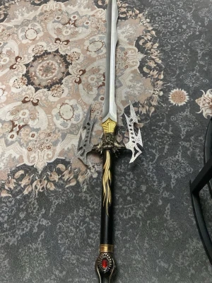 Fantasyinspirerat cosplaysvärd - Ett stort och detaljerat cosplaysvärd med silverfärgat blad, gulddetaljer och svart handtag med röd sten. Svärdet har dekorativa sidoblad och drakhuvud vid parerstången, perfekt för maskerad eller cosplay. Materialet är troligen metall och plast.