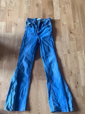 Blå utsvängda jeans Molly XS - Säljer ett par blå utsvängda Molly jeans från Gina Tricot i storlek XS. Jeansen har hög midja, klassisk femficksmodell och är tillverkade i stretchigt denimtyg. Perfekta för dig som gillar retrovibbar och en bekväm passform.