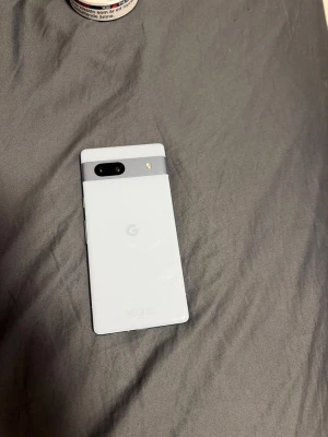 Ljus blå Google Pixel Android-telefon - Säljer en vit Google Pixel med stilren design och glasbaksida. Telefonen har en svart kamerarem med dubbla linser och LED-blixt. Framsidan är helsvart med tunna ramar och knappar på sidan. Perfekt för dig som gillar enkel och modern look. Kan gå ner i pris