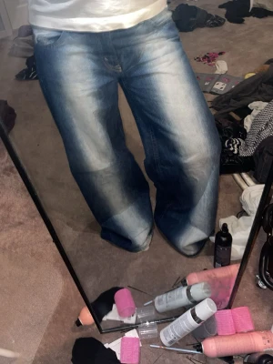 Blåa baggy jeans med bred passform - Säljer ett par blåa baggy jeans med bred passform och slitningar på låren. Jeansen har klassisk femficksmodell och låg midja. Perfekta för en avslappnad och trendig look.
