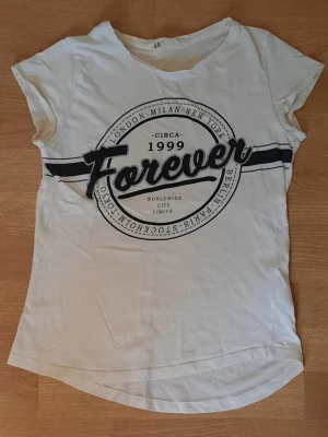 Vit t-shirt med tryck - Vit t-shirt med svart tryck från H&M. Trycket är lite glittrigt runt om. Den är i storlek 170 vilket motsvarar S. Materialet är bomull ☀️