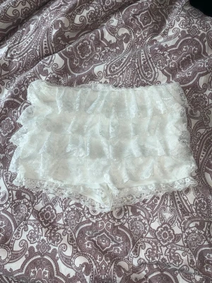 Vita spetsiga shorts - Supersöta vita shorts med flera lager volanger i spets. De har en mjuk och stretchig passform och är perfekta om du gillar romantisk och feminin stil. Shortsen är täckande och har fina spetsdetaljer runt hela kanten.