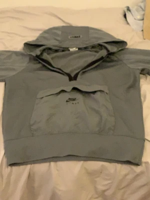 Grå Nike Air Max hoodie med huva - Snygg grå hoodie från Nike Air Max med stor magficka och huva. Hoodien har en klassisk passform och detaljer med Air Max-logga både på huvan och fickan. Perfekt för en avslappnad streetwear-look. Allt är bra förutom dragkedjan för att den är sönder.