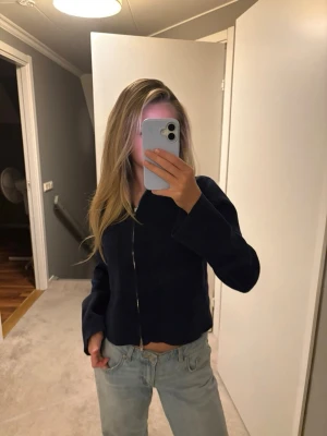 Mörkblå ziptröja med krage - Snygg mörkblå ziptröja med krage och raka ärmar. Tröjan har två stora fickor framtill och är något croppad i modellen. Perfekt att slänga över en t-shirt för en chill look. 