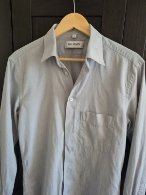 Balmain skjorta  - Snygg grå skjorta från Balmain med klassisk krage och bröstficka. Skjortan har lång ärm och knäppning framtill. Perfekt för dig som gillar stilrena plagg med exklusiv känsla.