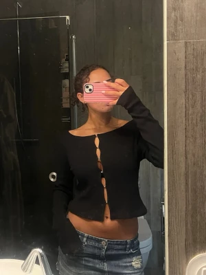 Svart ribbad topp från Weekday - Trendig svart ribbad topp från Weekday med öppen knappdetalj framtill. Toppen har en croppad passform och lång ärm, perfekt till jeans eller kjol. Använd fåtal gånger och i nästan nytt skick!!❤️‍🔥❤️‍🔥❤️‍🔥