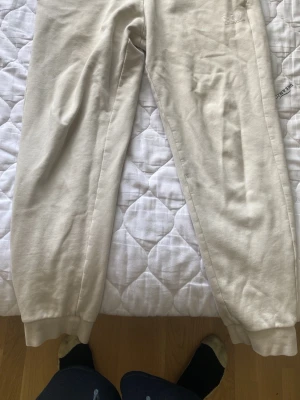 Beiga mjukisbyxor från EA7 - Säljer ett par beiga mjukisbyxor från EA7 Emporio Armani. Byxorna har resår i midjan och vid bensluten samt en broderad logga på benet. Tillverkade i mjukt bomullsmaterial som är skönt att ha på sig. Perfekta för chill dagar hemma eller när du vill vara bekväm.
