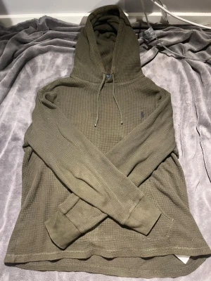 Olivgrön hoodie från Polo Ralph Lauren - Säljer en olivgrön hoodie från Polo Ralph Lauren med klassisk huva och dragsko. Tröjan har ett diskret broderat logotyp på bröstet och är tillverkad i ett mjukt, ribbat material som ger en avslappnad vibe. Perfekt för dig som gillar stilrena och bekväma plagg. Perfekt för någon som är hemma och vill ha en mjuk och skön outfit men samtidigt riktigt snygg. 🤩 