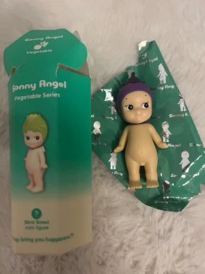 Sonny Angel Vegetable Series figur - Säljer en äkta söt samlarfigur från Sonny Angel Vegetable Series. Dockan har en lila mössa som liknar en aubergine och ett gulligt ansikte med stora ögon. Tillverkad i plast och kommer med originalförpackning och papper.