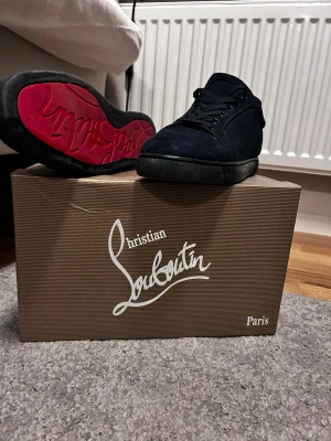 Blåa sneakers från Christian Louboutin - Snygga navy blåa sneakers från Christian Louboutin med klassisk röd sula och blåa skosnören. Skorna är låga och har en ovandel i mocka med diskreta detaljer. Perfekta för dig som vill sticka ut med en exklusiv touch.   Pris kan diskuteras 