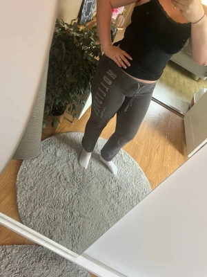 Grå mjukisbyxor med tryck - Säljer ett par grå mjukisbyxor med vitt tryck längs ena benet och dragsko i midjan. Byxorna har en avslappnad passform och är perfekta för chill dagar hemma. Materialet är mjukt och stretchigt för extra komfort. Har dock några hål men är fina och går att sy.
