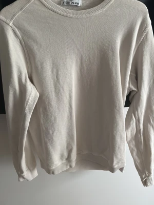 Beige sweatshirt från Stone Island - Säljer en stilren beige sweatshirt från Stone Island. Tröjan har rund halsringning, långa ärmar och ribbade muddar vid ärmslut och nederkant. Perfekt för en clean och avslappnad look. Materialet är mjukt och bekvämt, troligtvis bomull. Perfekt till en lite svalare sommarkväll är öppen för förhandling 