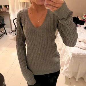 tommy hilfiger tröja grå - grå kabelstickad tröja från tommy hilfiger i storlek S. tröjan har en djupt v-ringad hals, långa ärmar och ribbade muddar. klassisk logga på ärmen💞