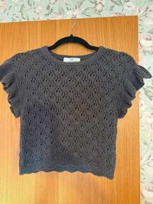 Mörkgrå stickad topp med volangärm - Snygg mörkgrå stickad topp från H&M med korta volangärmar och ett genombrutet spetsmönster. Är i storlek 146/152