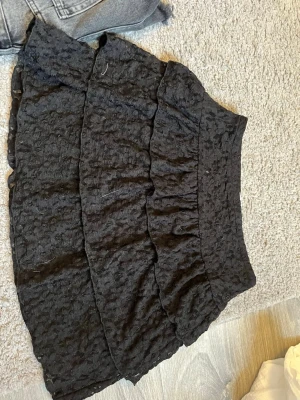 Svart volangkjol med spetsdetaljer - Säljer en svart kjol med flera volanger och fina spetsdetaljer. Kjolen har en hög midja och kort modell, perfekt för dig som gillar en trendig och feminin stil. Materialet är lätt och ger kjolen ett snyggt fall.