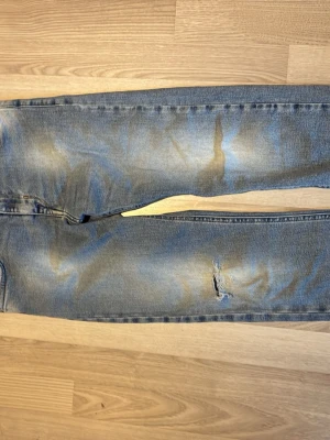 Blåa jeans Reaplay - Ett par blå jeans med rak passform och och Jeansen har klassisk femficksdesign, ljus tvätt och ett litet hål på ena benet för en trendig look. Materialet är denim i bomull. Perfekta för en avslappnad stil. Men höger ficka i fram har ett hål