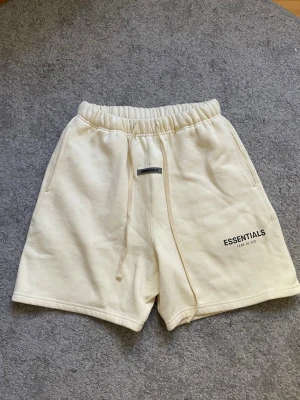 Essentials shorts beige - Snygga beige shorts från Essentials Fear of God med elastisk midja och snörning. Shortsen har två sidofickor, en bakficka och logga tryckt på vänster ben. Perfekta för sommaren! Pris kan diskuteras 