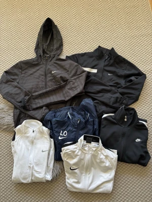 6-Pack Nike vindjackor/Träningsjackor och Träningströjor - Säljer ett gäng snygga Nike jackor o tröjor i olika modeller och färger. Här finns både svarta, vita och en marinblå vindjacka, flera med dragkedja och sportig look. Perfekta för träning eller chill. Klassiska Nike-loggor på bröstet och vissa har huva.