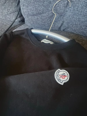 Svart Moncler sweatshirt - Svart sweatshirt från Moncler med rund halsringning och klassisk passform. Tröjan har Moncler-logga broderad på armen och är tillverkad i mjukt material. Perfekt för en stilren och enkel look.
