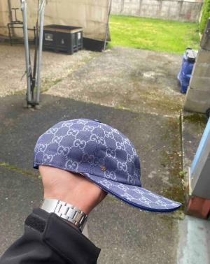 Blå Gucci keps med monogram - Snygg blå keps från Gucci med klassiskt GG-monogram i vitt över hela kepsen. Kepsen har böjd skärm och är tillverkad i ett tygmaterial som känns både lyxigt och trendigt. Perfekt accessoar för att lyfta din streetwear-look.