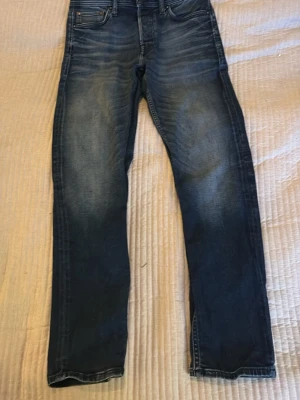 Blå jeans från Jack & Jones - Snygga blå jeans från Jack & Jones med klassisk femficksmodell och lätt slitna detaljer framtill. Modellen heter Comfort Mike och har en rak passform som ger en avslappnad look. Perfekta till vardags för en stilren och bekväm outfit. W28 l30