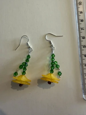 Blommiga örhängen med pärlor - Unika örhängen formade som blommor i gult och grönt. De är handgjorda med gröna och bruna pärlor samt blommor i plast. Krokar i metall. Perfekta för dig som gillar färgglada och lekfulla accessoarer. Nickelfria 