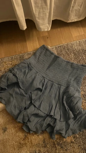 Blå volangkjol från SHEIN - Supersöt blå kortkjol från SHEIN med bred smock i midjan och flera lager volanger. Kjolen har en luftig och lätt struktur som ger en avslappnad men ändå trendig look. Perfekt att styla med en enkel topp för en cool outfit.