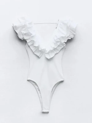 Vit body med volang och v-ringning - Supersnygg vit body med djup V-ringning och stora volanger längs axlar och halsringning. Tillverkad i stretchigt material som sitter tajt och bekvämt. Perfekt för dig som gillar en feminin och trendig look.