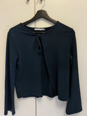 Mörkblå omlottkofta från 157 - Mörkblå omlottkofta från 157 med knytband vid halsen. Koftan har långa ärmar och är tillverkad i ett mjukt, stretchigt material som ger en skön passform. Perfekt för lager på lager och enkel att styla till olika outfits.