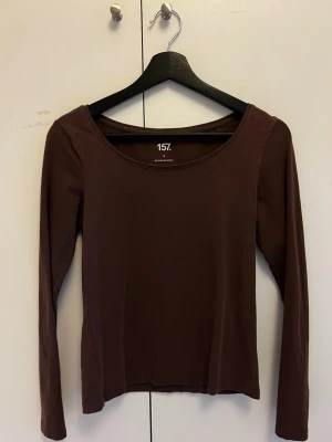 Brun långärmad topp från 157 - Mörkbrun långärmad topp från 157 med rund halsringning. Tillverkad i mjuk bomull med lite stretch för en bekväm passform. Perfekt att styla med jeans eller kjol för en enkel och snygg look.