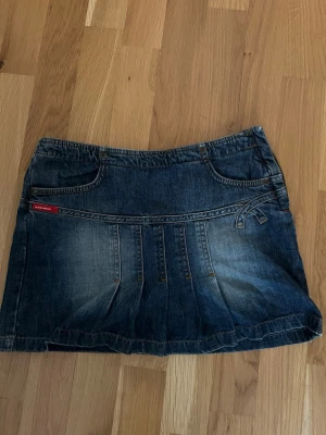 Mörkblå jeanskjol med fickor - Säljer en mörkblå jeanskjol från Crocker med klassiska fickor fram och bak samt dekorativa sömmar. Kjolen har en kort modell och är gjord i slitstarkt denimtyg. Perfekt till sneakers eller boots för en cool vardagslook.