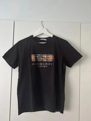 Svart t-shirt med rutigt tryck. - Snygg svart t-shirt med klassiskt rutigt tryck och logga på bröstet T-shirten har rund hals och korta ärmar, säljer eftersom den inte kommer till användning mer. ( pris kan diskuteras )