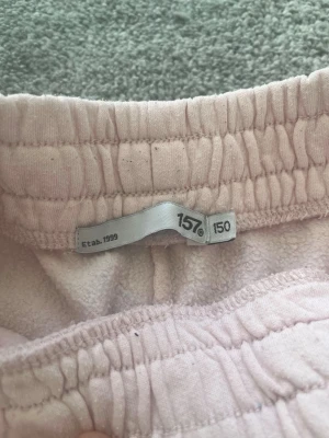 Ljusrosa mjukisbyxor från 157 - Ljusrosa mjukisbyxor från 157 med resår i midjan och två bakfickor. Byxorna har en rak passform och är gjorda i ett mjukt, fleeceliknande material som är skönt mot huden. Perfekta för en avslappnad stil.