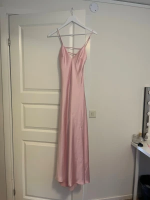 Lång satinklänning - Elegant långklänning i ljusrosa satin med smala axelband och v-ringning. Klänningen har en öppen rygg. Kan tänka mig gå ner i pris vid snabb affär.