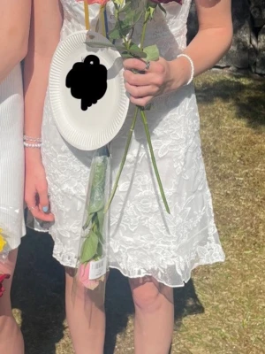Vit spetsklänning med v-ringning - Säljer en vit kortklänning med v-ringning och korta ärmar. Klänningen har ett vackert blommigt spetsmönster och en feminin passform. Perfekt för student eller sommarens alla tillfällen. 