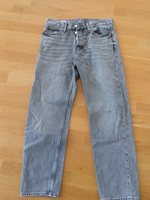 Grå raka jeans med knappgylf - Säljer ett par grå jeans från H&M med raka ben och klassisk femficksdesign. Jeansen har knappgylf och är tillverkade i denim. Perfekta för dig som gillar en enkel och tidlös look. Storlek 32/30 i längd och midja. Ser oanvända ut.