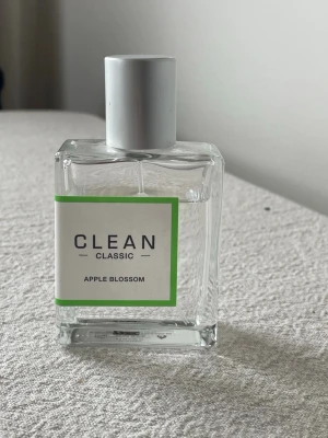 CLEAN Classic Apple Blossom parfym - Fräsch parfym från CLEAN i doften Apple Blossom. Flaskan är rektangulär i genomskinligt glas med en stilren vit etikett och grön ram. Locket är silverfärgat och flaskan rymmer 60 ml eau de parfum. Perfekt för dig som gillar lätta, fruktiga dofter.