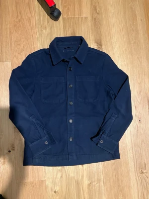 Mörkblå overshirt med fickor - Donce de la sense overshirt, fickor på bröstet, mörkblå, knappar hela vägen upp, tryck vid nacken på insidan, tryck nere på armen, nypris 1599kr, inga skador. 