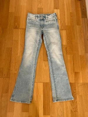Ljusblå bootcut jeans - Säljer ett par ljusblå bootcut jeans med slitna detaljer och klassisk femficksmodell. Jeansen har låg midja och utsvängda ben!