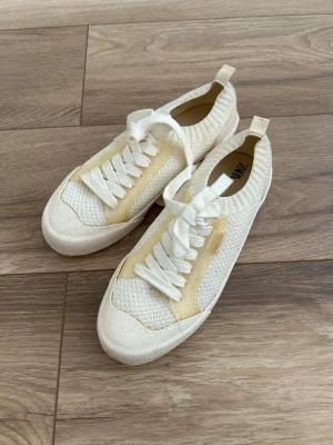 Beige stickade sneakers från Zara - Säljer ett par ljusbeige sneakers med stickad ovandel från Zara barn i storlek 38. Skorna har vita snören och ribbad kant runt ankeln. Använda kort vid ett tillfälle. 