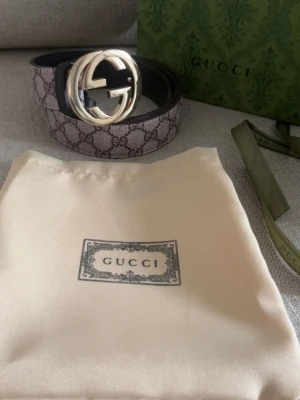 GG Supreme bälte med guldspänne - Säljer ett klassiskt GG Supreme bälte med ikoniskt guldigt GG-spänne. Bältet har det välkända monogrammönstret i beige och brunt och är tillverkat i canvas med detaljer i skinn. Perfekt accessoar för att lyfta vilken outfit som helst.