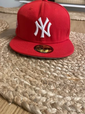 Röd New Era Yankees keps - Snygg röd keps från New Era med New York Yankees-logga broderad i vitt framtill. Klassisk flat brim och ikonisk sticker på skärmen. Tillverkad i bomullsmix och har New Era-logga på sidan. Perfekt för dig som vill sticka ut med en sportig och trendig stil.