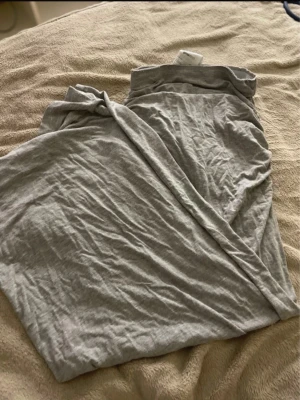 Grå mjuk pyjamasbyxa med rynk - Säljer ett par gråa pyjamasbyxor i mjukt och stretchigt material. Byxorna har en avslappnad passform och en snygg rynkad detalj längs ena sidan som ger en unik touch. Perfekta för chill dagar hemma.