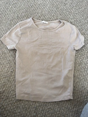 Beige basic t-shirt i bomull - En enkel och stilren beige t-shirt med rund hals och korta ärmar. Perfekt att matcha med jeans eller shorts för en clean look. Tillverkad i mjuk bomull som känns skön mot huden.